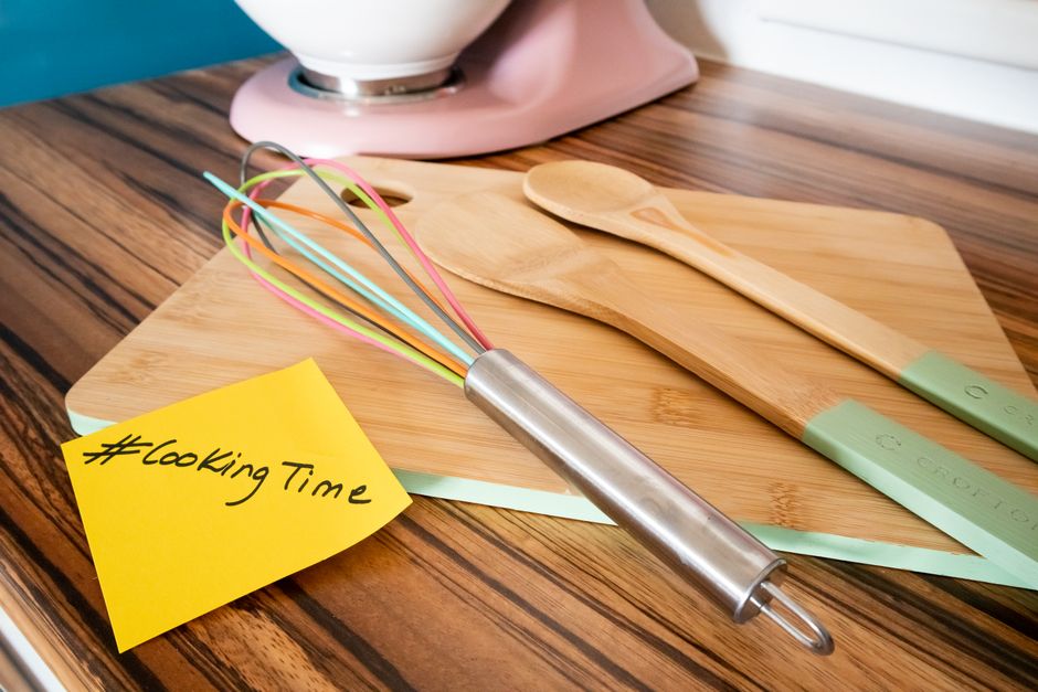 Colorful kitchen utensils on a bamboo cutting board with a cooking hashtag note, perfect for culinary themes.