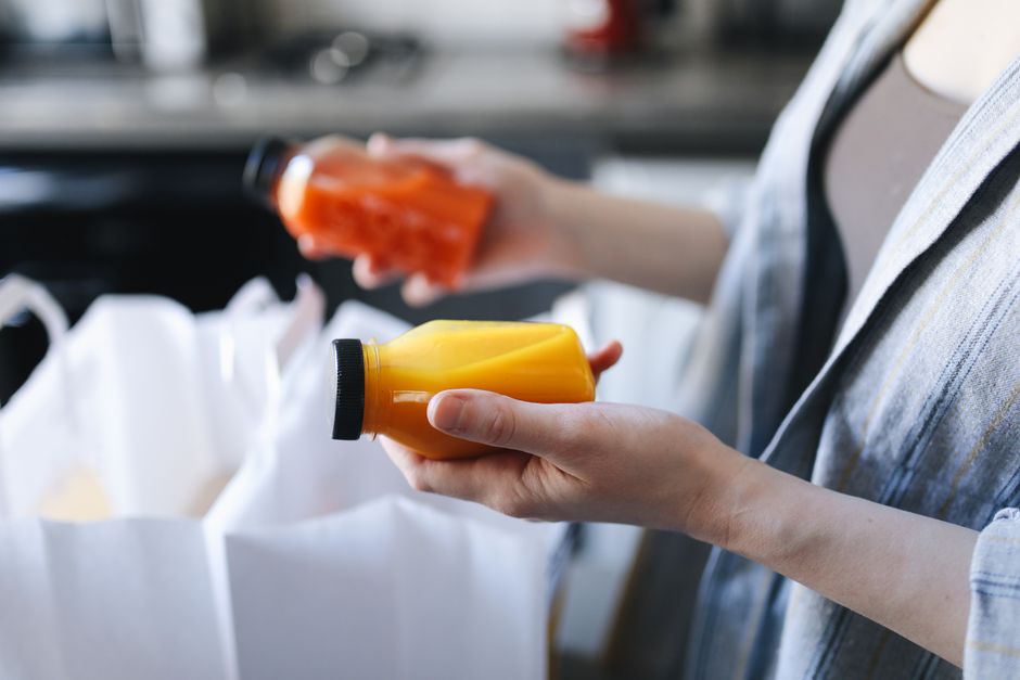 A person holding two juice bottles, inspecting options in a kitchen setting.